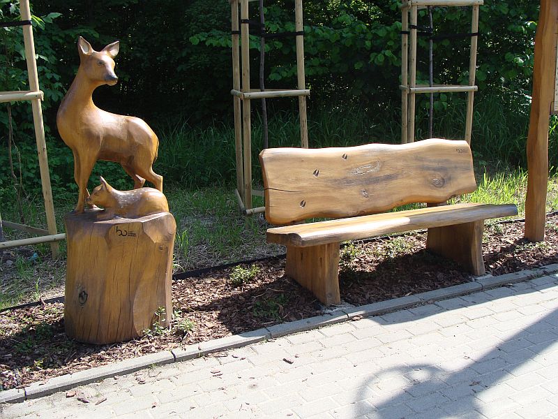 ławeczka na ulicy Lipnickiej a obok niej drewniana rzeźba sarny